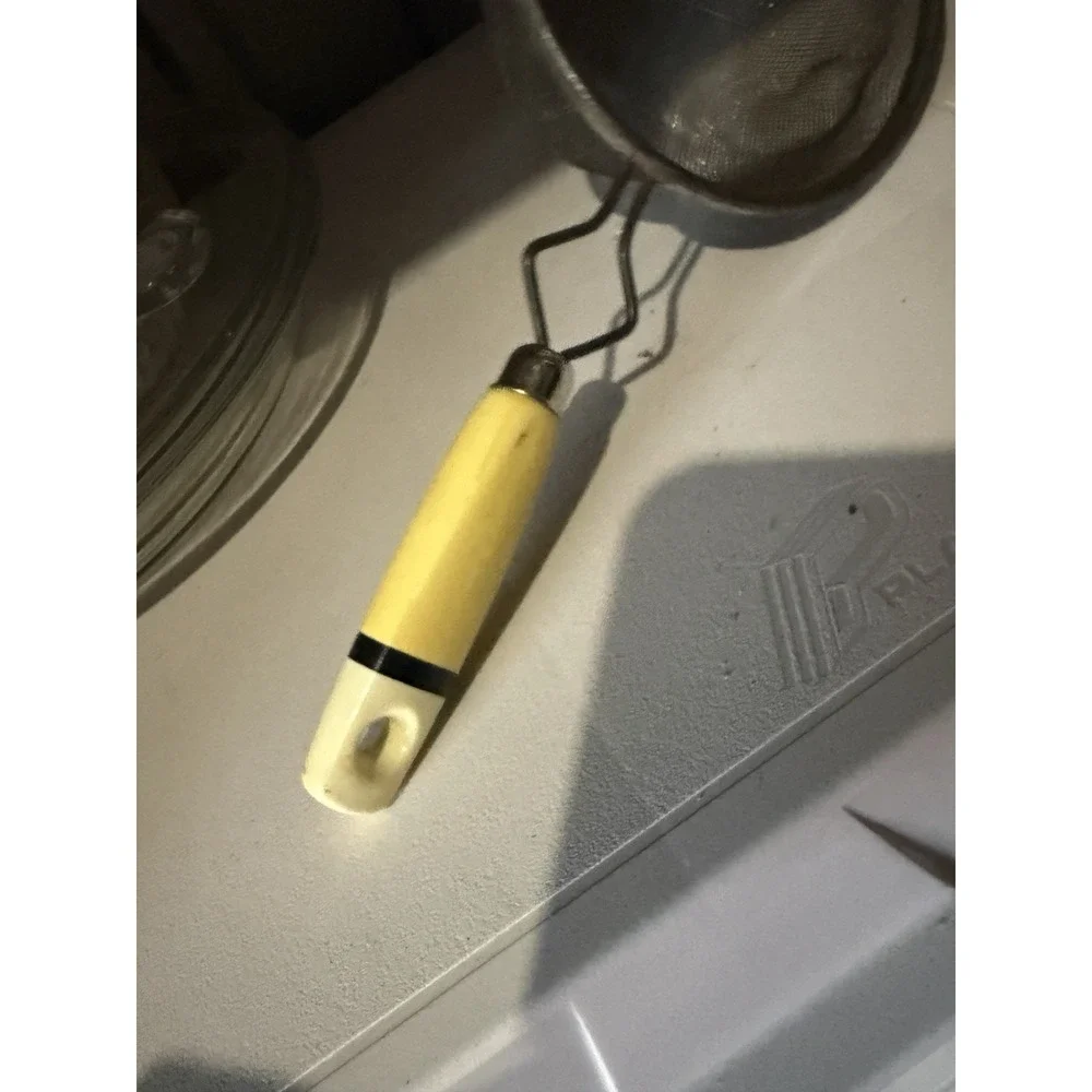 The vintage Eckoline hand-held mesh strainer with a yellow and white plastic